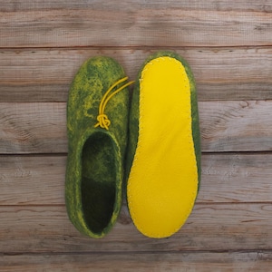 May include: A pair of green felt slippers with yellow felt soles. The slippers have a yellow tassel on the top.