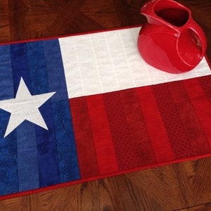 Könnte beinhalten: Ein Tischläufer in den Farben Rot, Weiß und Blau mit der Flagge von Texas. In der blauen Sektion befindet sich ein weißer Stern. Der Läufer ist aus Stoff und hat eine gesteppte Textur.