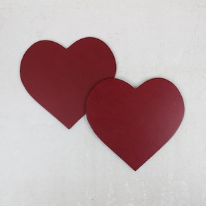 May include: Two red heart-shaped coasters. The coasters are made of a smooth, solid material.