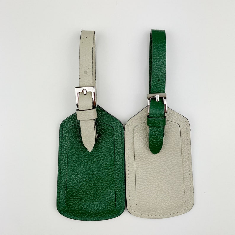May include: Two leather luggage tags, one green and one beige, with silver buckles. The tags are blank and ready to be personalized.