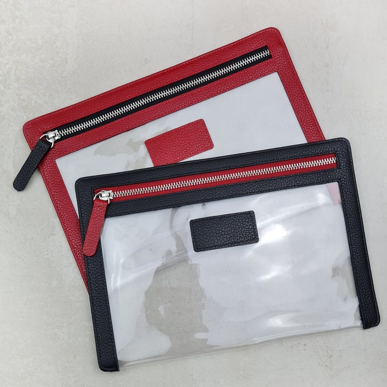May include: Two rectangular pouches with clear plastic centers and textured borders. One pouch features a red border with a matching red tab, while the other has a black border with a matching black tab. Both include silver metal zippers.