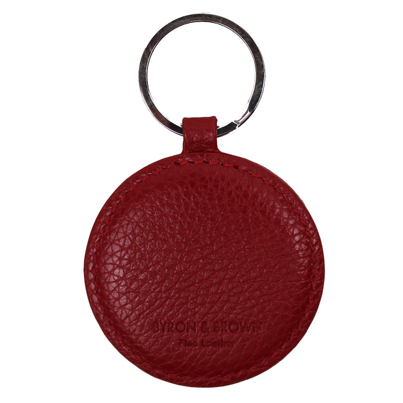 May include: Red leather keychain with a round, textured design. The keychain features a silver key ring and the text "Byron & Brown Fine Leather" embossed on the front.