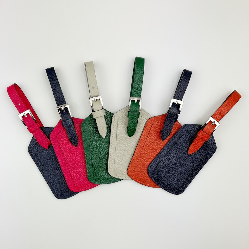 May include: Six leather luggage tags in different colors, including green, red, blue, white, and orange. Each tag has a silver buckle.