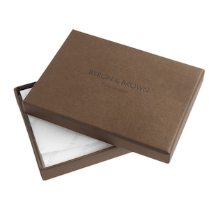 Puede incluir: Una caja marr&oacute;n con el texto "BYRON & BROWN Fine Leather" en la parte superior. La caja est&aacute; abierta y el interior est&aacute; forrado con papel de seda blanco.