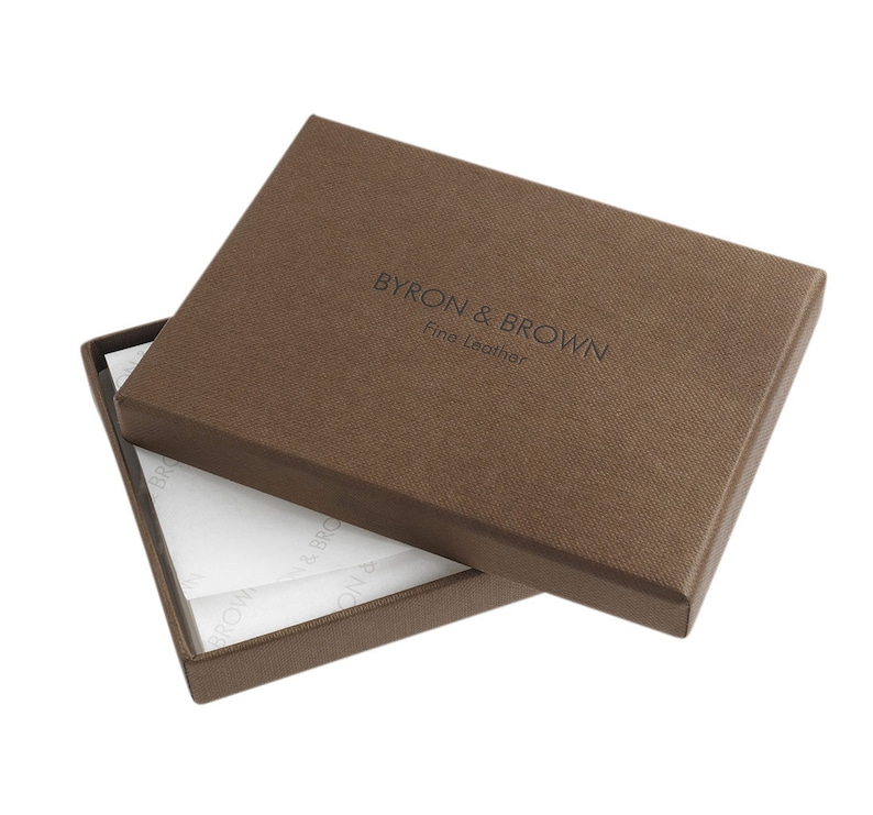Puede incluir: Una caja marr&oacute;n con el texto "BYRON & BROWN Fine Leather" en la parte superior. La caja est&aacute; abierta y el interior est&aacute; forrado con papel de seda blanco.