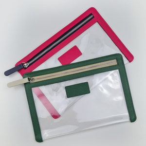 May include: Two rectangular pouches with clear centers and textured borders. One pouch features a hot pink border with a dark blue zipper pull, while the other has a forest green border with a beige zipper pull and a matching rectangular patch.