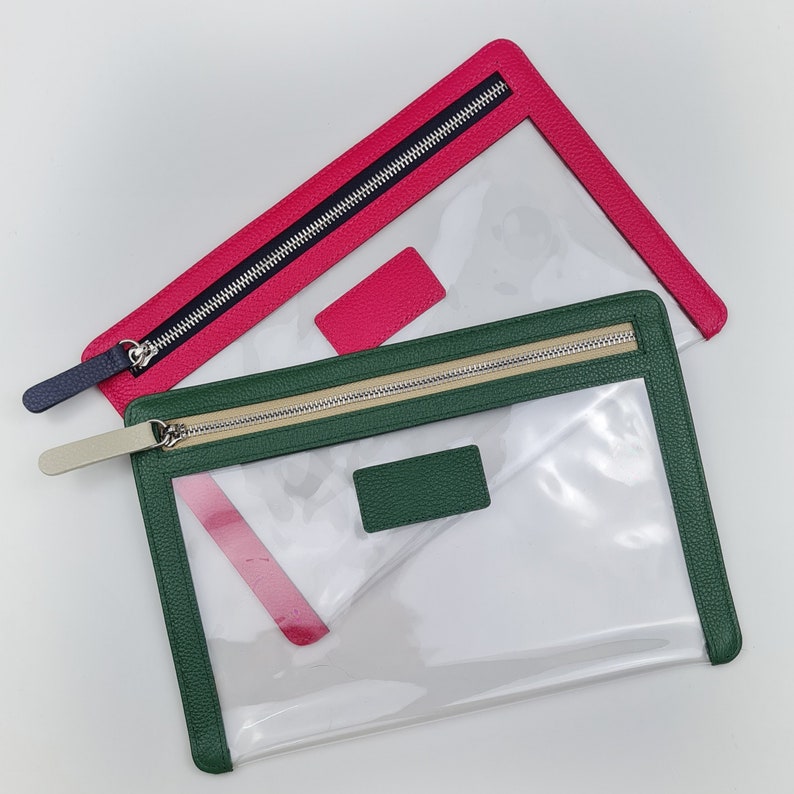 May include: Two rectangular pouches with clear centers and textured borders. One pouch features a hot pink border with a dark blue zipper pull, while the other has a forest green border with a beige zipper pull and a matching rectangular patch.
