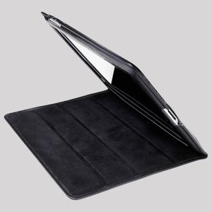 Könnte beinhalten: Schwarze Tablet-Hülle mit einem Klappdeckel. Die Hülle ist geöffnet und zeigt den Bildschirm und das Innenfutter. Der Deckel hat eine strukturierte, matte Oberfläche und das Innere eine weiche, Wildleder-ähnliche Textur. Die Hülle dient zum Schutz eines Tablets.