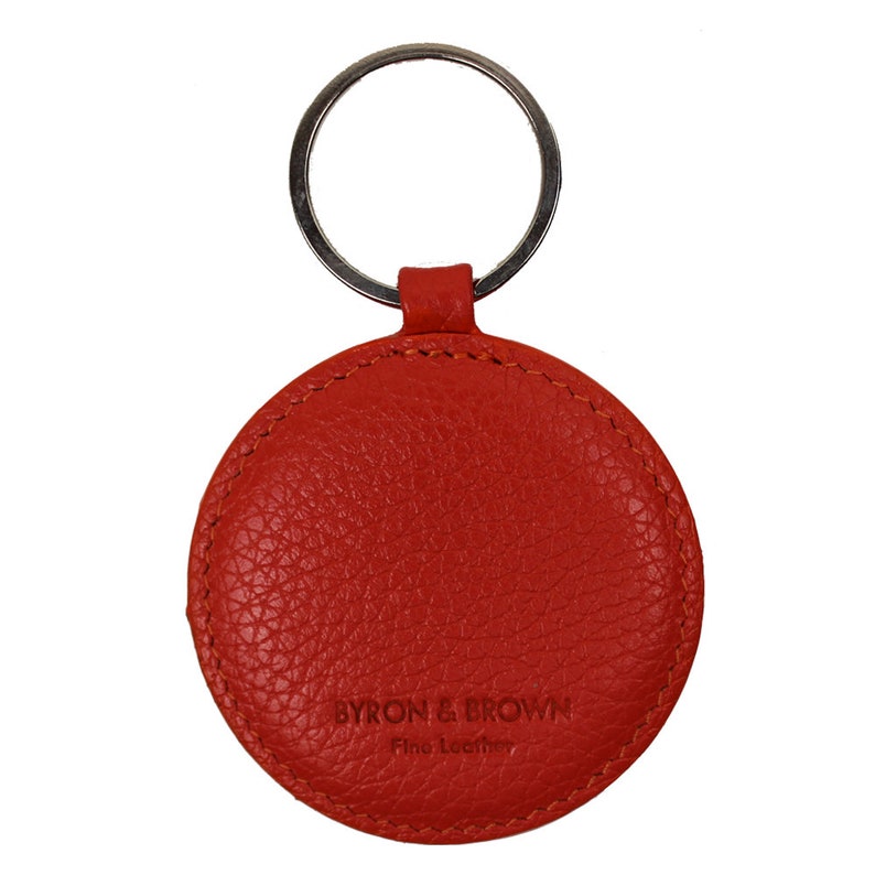 May include: A round, bright orange leather keychain with a silver key ring. The keychain has the text "BYRON & BROWN Fine Leather" embossed on the front.