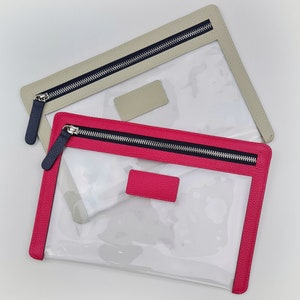 May include: Two rectangular pouches with clear plastic bodies and textured leather-like trim. One pouch features a bright pink border and matching rectangular patch, while the other has a beige border and patch. Both include dark navy zippers.