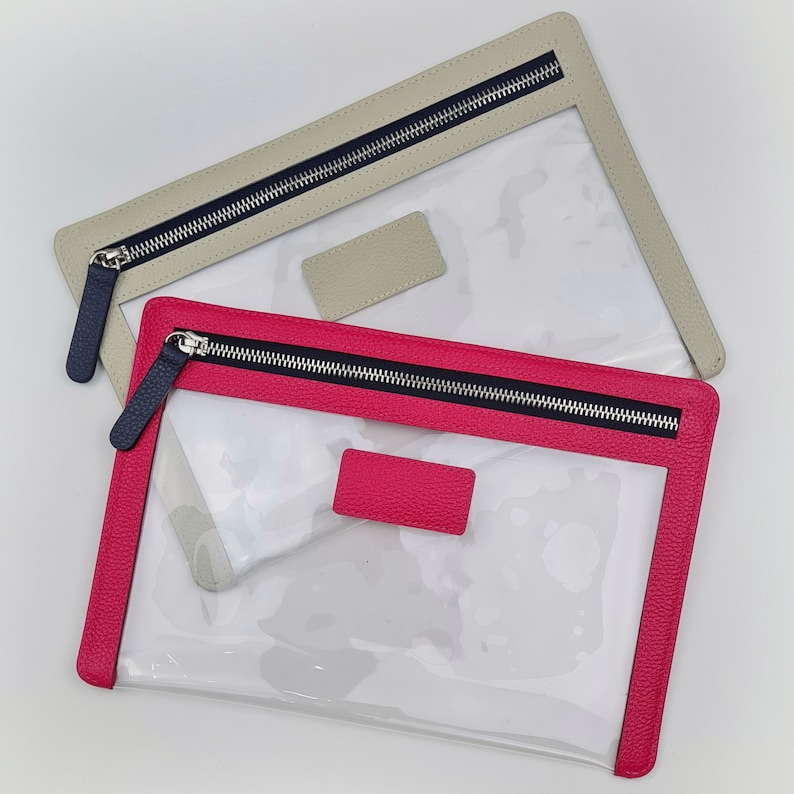May include: Two rectangular pouches with clear plastic bodies and textured leather-like trim. One pouch features a bright pink border and matching rectangular patch, while the other has a beige border and patch. Both include dark navy zippers.
