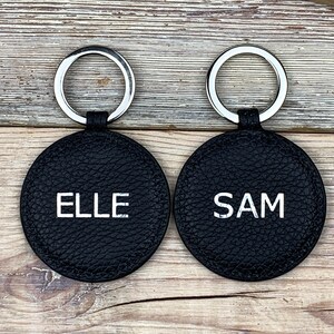 May include: Two black leather keychains with silver key rings. The keychains are round and have the names "ELLE" and "SAM" embossed in white lettering.