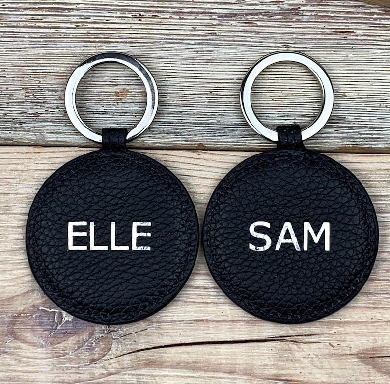 May include: Two black leather keychains with silver key rings. The keychains are round and have the names "ELLE" and "SAM" embossed in white lettering.