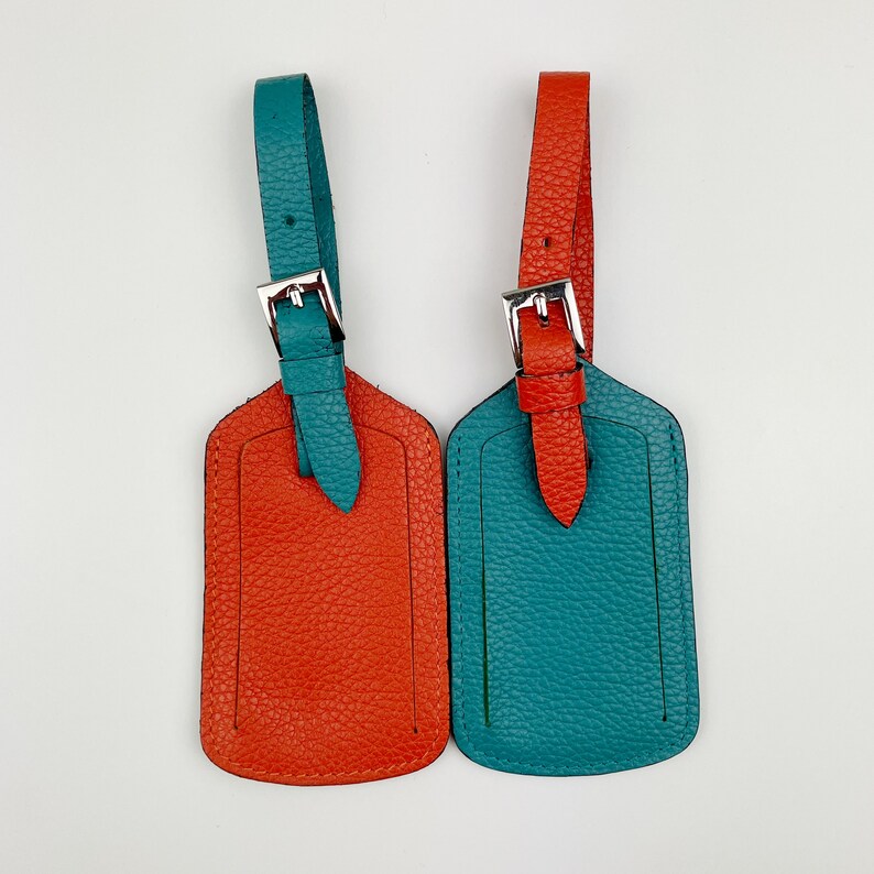May include: Two leather luggage tags, one orange and one teal, with silver buckles and loops.