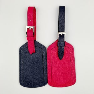 May include: Two leather luggage tags, one navy blue and one bright pink. Both tags have a silver buckle and a loop for attaching to luggage.