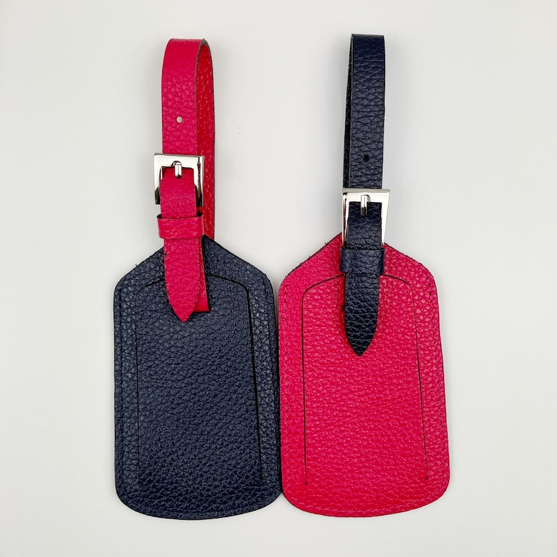 May include: Two leather luggage tags, one navy blue and one bright pink. Both tags have a silver buckle and a loop for attaching to luggage.