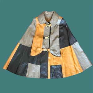 May include: A patchwork leather cape in shades of brown, tan, black, and orange. The cape has a collar and three gold-coloured clasps down the front. The design is a mix of geometric shapes and textures.