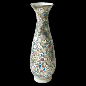 Może przedstawiać: Wysoki, dekoracyjny wazon z wąską szyjką i rozszerzoną krawędzią. Wazon zdobiony jest kolorowymi motywami kwiatowymi i króliczymi, z teksturowanym, metalicznym wykończeniem. Podstawa ma jaśniejszy kolor niż korpus wazonu.