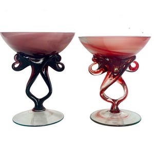 May include: Two glass bowls with swirling red and white patterns. The bowls have unique, twisted, black and red stems.