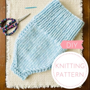 May include: A light blue knitted blanket with a DIY knitting pattern label. The blanket is laid out on a white, fluffy surface.
