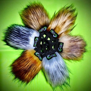 Puede incluir: Colección de seis accesorios de piel sintética en varios colores, incluyendo marrón, blanco y gris, dispuestos en forma circular. Cada pieza está unida a una correa negra con un logotipo verde y blanco.