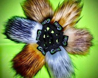 Peut inclure: Ensemble de six accessoires en fausse fourrure de différentes couleurs, dont marron, blanc et gris, disposés en cercle. Chaque pièce est fixée à une sangle noire avec un logo vert et blanc, sur fond vert.
