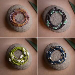 May include: Four different beaded waist beads, each on a gray stone. The beads are in various colors and patterns, including brown, green, white, and blue.