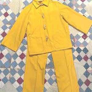 May include: A yellow two-piece outfit with a long-sleeved jacket and pants. The jacket has a collar and wooden toggle closures. The pants have a straight leg.