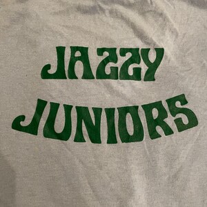 Może przedstawiać: Szary T-shirt z nadrukiem "Jazzy Juniors" w kolorze zielonym.