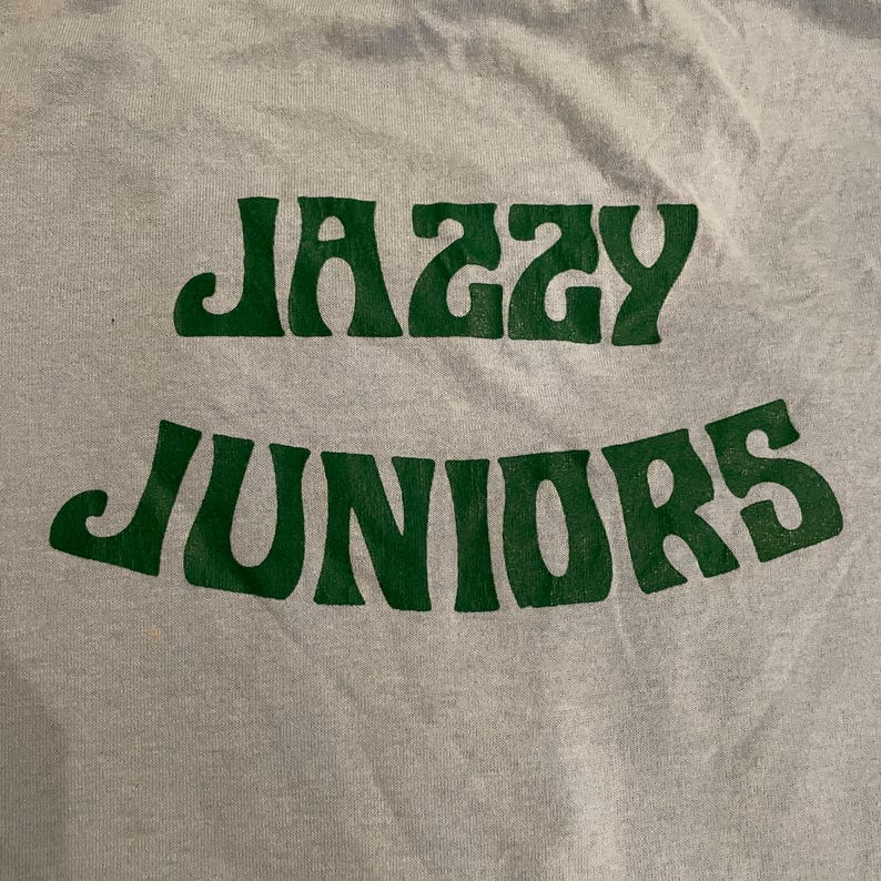 Może przedstawiać: Szary T-shirt z nadrukiem "Jazzy Juniors" w kolorze zielonym.