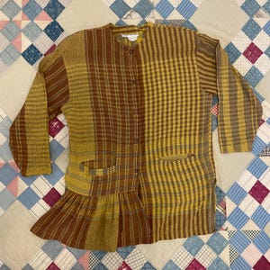 May include: A brown and yellow plaid button-up shirt with a ruffled hem. The shirt has two pockets and a collar.