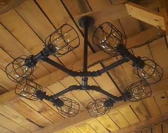 May include: A black metal pipe chandelier with six caged light bulbs. The chandelier is mounted on a wooden ceiling.