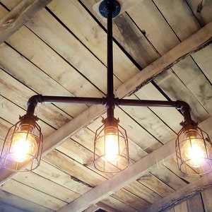 May include: A three-light industrial style pendant light fixture with black metal pipes and caged bulbs. The fixture is mounted on a wooden ceiling.
