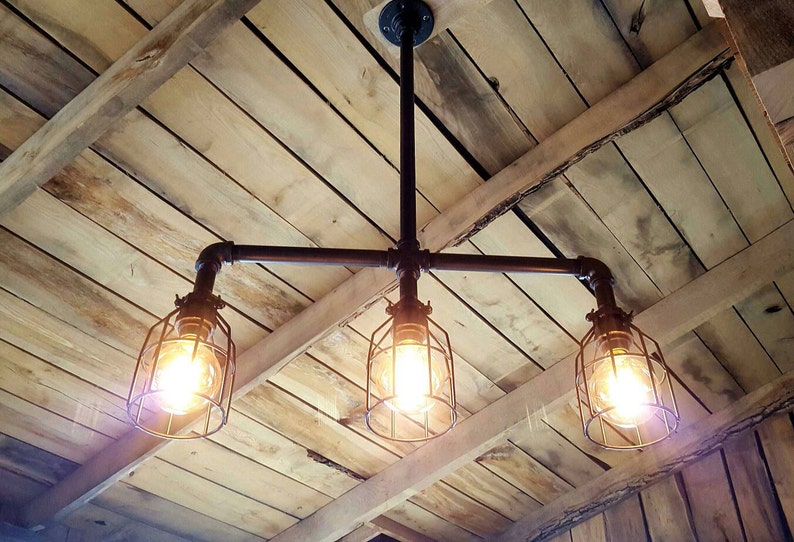 May include: A three-light industrial style pendant light fixture with black metal pipes and caged bulbs. The fixture is mounted on a wooden ceiling.