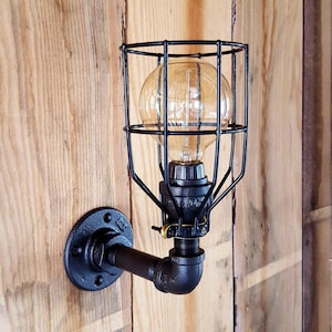 May include: Black industrial style wall sconce with a caged light bulb. The sconce is made of metal pipe and has a black finish.