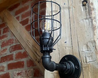 May include: Black industrial style wall sconce with a cage light fixture and a pipe arm. The sconce is mounted on a wooden beam.
