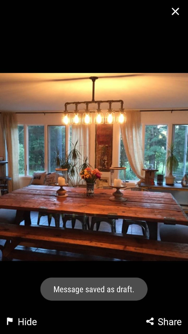 May include: A rustic wooden dining table with a long, rectangular top and a bench seat. The table is lit by a six-light industrial-style chandelier with exposed pipes and clear glass bulbs.