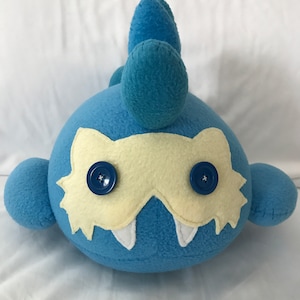 May include: Blue plush toy with a yellow mask and two blue buttons for eyes. The toy has a spiky blue tail.