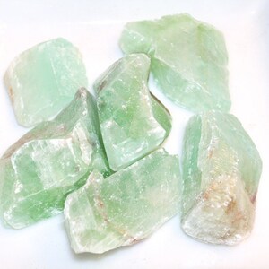 May include: A collection of six green, translucent, rough-cut, natural stones. The stones are various sizes and shapes.