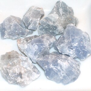 May include: A collection of seven blue celestite crystal stones. The stones are rough and have a natural, unpolished look.