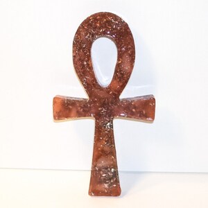 May include: A brown and gold Ankh symbol made of resin with glitter embedded in the resin.