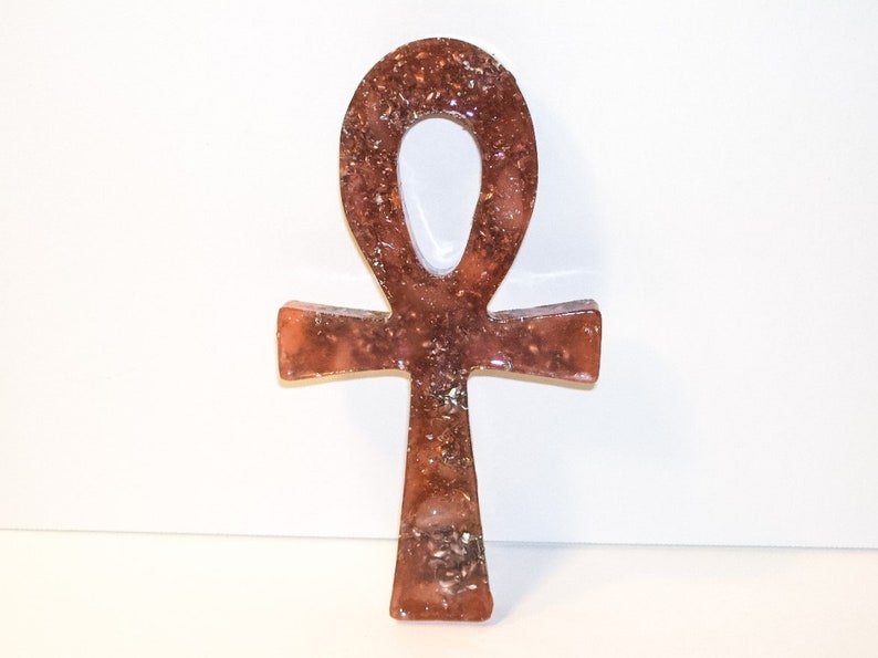 May include: A brown and gold Ankh symbol made of resin with glitter embedded in the resin.