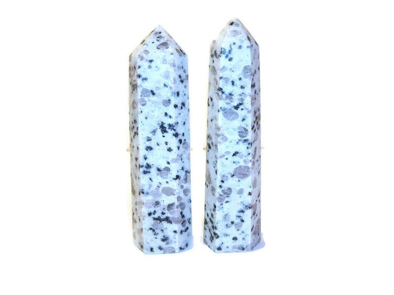 May include: Two tall, polished stone obelisks. The obelisks are white with gray and black speckled patterns. They have a faceted design and a pointed top. The background is plain white.