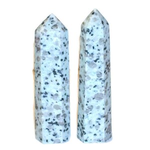 May include: Two polished, light-colored stone obelisks with a speckled pattern of gray and black dots. The obelisks have a pointed top and a rectangular base. The background is plain white.