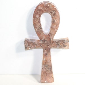 May include: A pink and silver Ankh symbol made of resin with embedded glitter. The Ankh is a symbol of life and eternal life in ancient Egyptian culture.