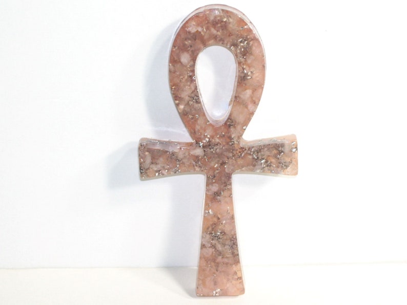 May include: A pink and silver Ankh symbol made of resin with embedded glitter. The Ankh is a symbol of life and eternal life in ancient Egyptian culture.