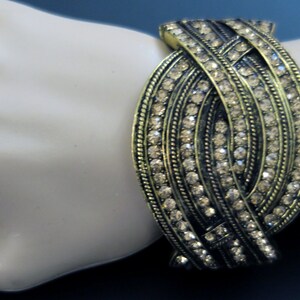 May include: A gold-toned bracelet with a woven design and clear rhinestones.