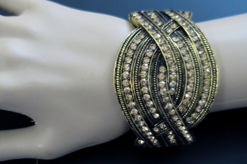 May include: A gold-toned bracelet with a woven design and clear rhinestones.