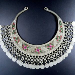 Può includere: Una collana d'argento a forma di mezzaluna con una frangia di monete d'argento. La collana è decorata con pietre preziose rosse e verdi.