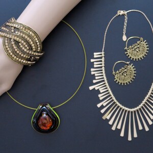 May include: A set of gold-tone jewelry featuring a necklace with a fringe design, a pair of earrings with a circular filigree design, and a bracelet with a multi-layered design with rhinestones.